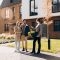 Happy couple smiling as professional real estate agent hands them house keys, celebrating successful purchase and new home ownership in sunny residential neighborhood. Business concept